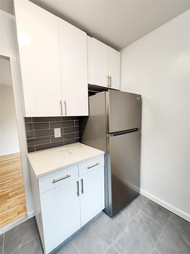 kitchen featuring white cabinetry, backsplash, light stone counters, and stainless steel fridge