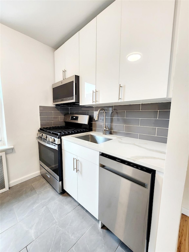 kitchen featuring sink, appliances with stainless steel finishes, light stone countertops, white cabinets, and decorative backsplash