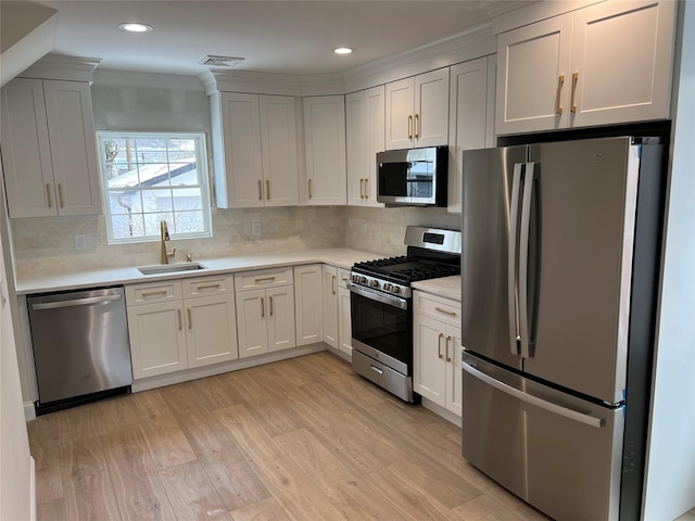 kitchen with appliances with stainless steel finishes, light wood-type flooring, decorative backsplash, sink, and white cabinetry