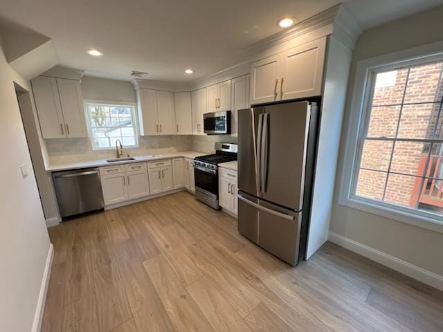 kitchen with appliances with stainless steel finishes, light hardwood / wood-style floors, sink, white cabinetry, and backsplash