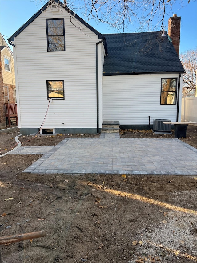 rear view of house featuring roof with shingles, cooling unit, a patio, and a chimney