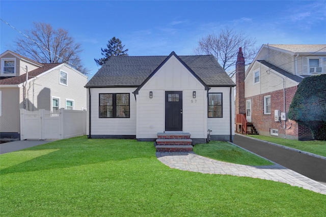 view of front of property with roof with shingles, board and batten siding, entry steps, a front yard, and fence