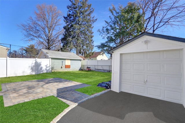 view of yard with an outbuilding, a patio, a fenced backyard, a garage, and driveway