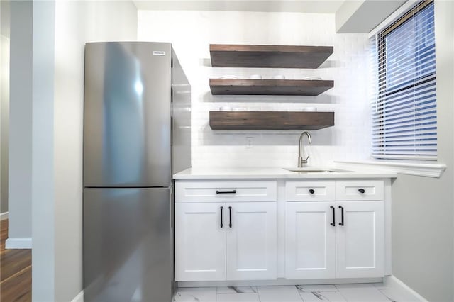 kitchen with white cabinetry, stainless steel refrigerator, and sink