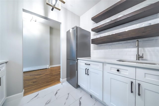 kitchen featuring sink, light hardwood / wood-style flooring, a baseboard heating unit, stainless steel fridge, and white cabinets