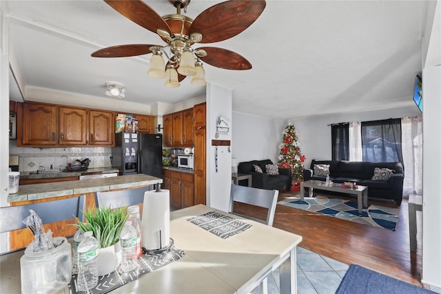 kitchen with ceiling fan, tasteful backsplash, tile counters, light hardwood / wood-style floors, and black fridge with ice dispenser