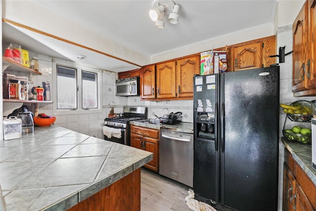 kitchen with stainless steel appliances, crown molding, tile walls, light hardwood / wood-style floors, and tile counters