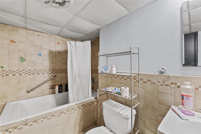 bathroom featuring a paneled ceiling, shower / bath combo with shower curtain, tile walls, and toilet