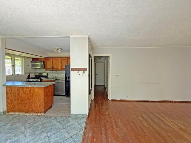 33 Birch Ct, Riverhead, NY 11901 - kitchen featuring stainless steel appliances, brown cabinets, a peninsula, a textured ceiling, and light wood-style floors