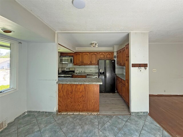 33 Birch Ct, Riverhead, NY 11901 - kitchen featuring stainless steel appliances, brown cabinetry, a peninsula, a textured ceiling, and tasteful backsplash