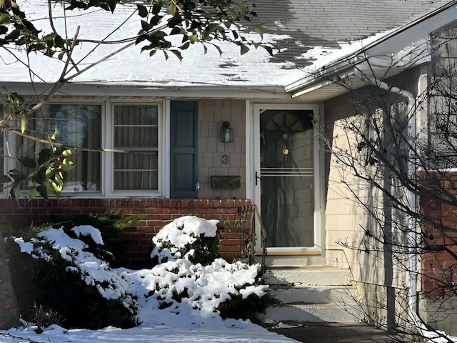 snow covered property entrance featuring brick siding