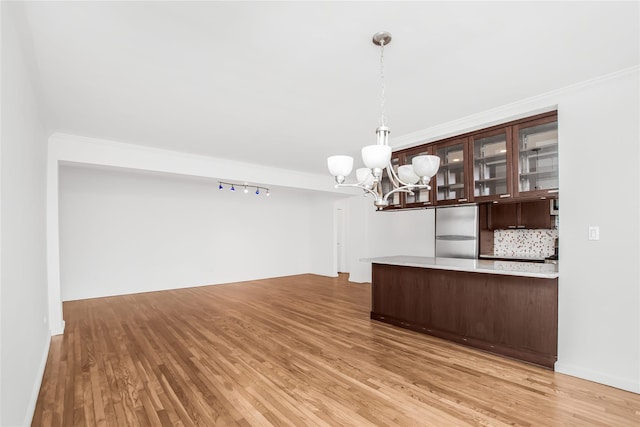 interior space with stainless steel built in fridge, backsplash, light wood-style floors, and an inviting chandelier