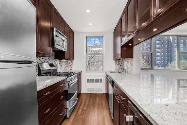 kitchen featuring dark brown cabinetry, wood finished floors, light stone countertops, stainless steel appliances, and a sink