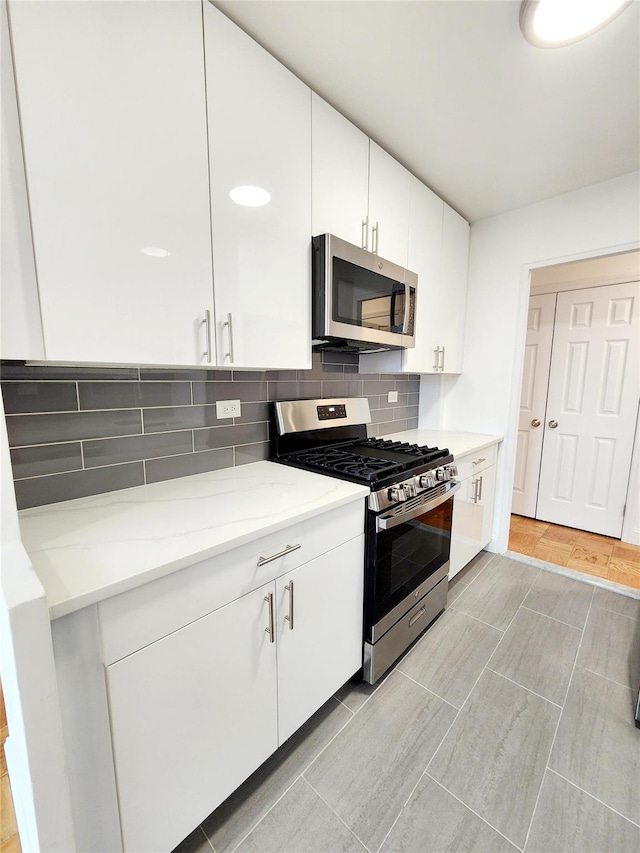 kitchen featuring decorative backsplash, stainless steel appliances, white cabinets, and light stone counters