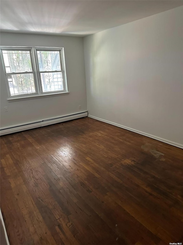 empty room with dark wood-type flooring and a baseboard heating unit