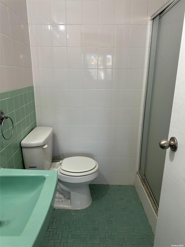 bathroom featuring tile patterned flooring, a shower with door, tile walls, and toilet