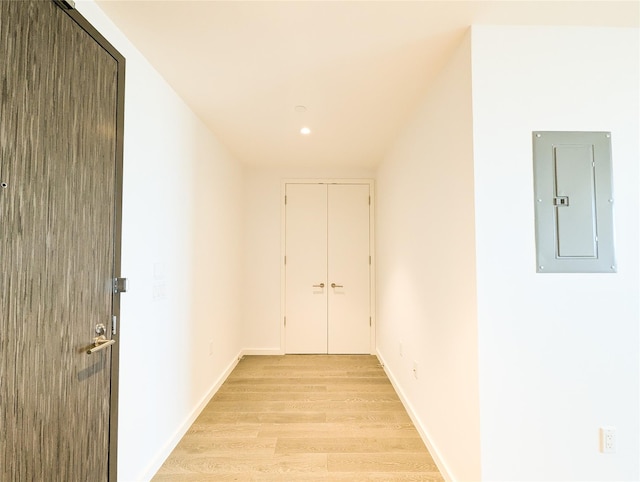 corridor with light wood finished floors, electric panel, and baseboards