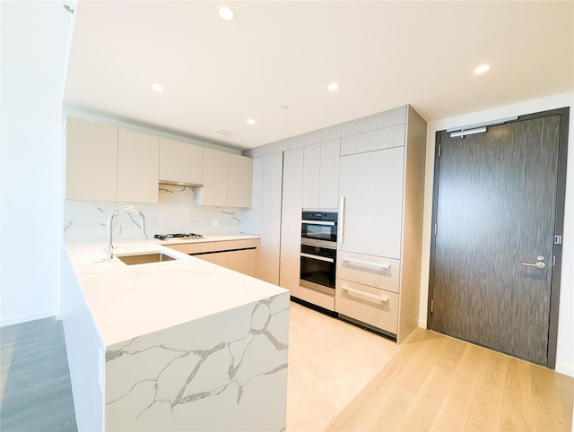 kitchen featuring recessed lighting, a peninsula, a sink, light wood-style floors, and light stone countertops