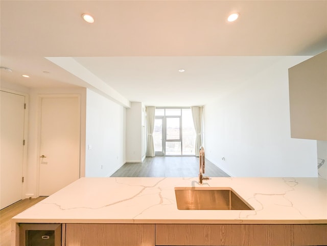 kitchen with light wood-type flooring, recessed lighting, a sink, and light stone countertops