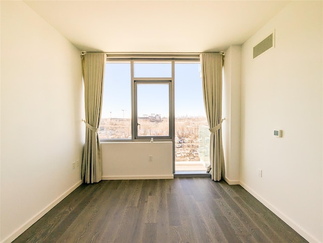 empty room with dark wood-style floors, baseboards, and visible vents