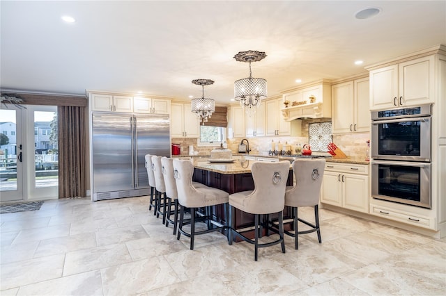 kitchen with cream cabinets, hanging light fixtures, light stone countertops, appliances with stainless steel finishes, and a kitchen island