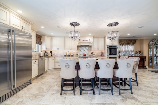 kitchen with cream cabinetry, pendant lighting, stainless steel appliances, and light stone countertops