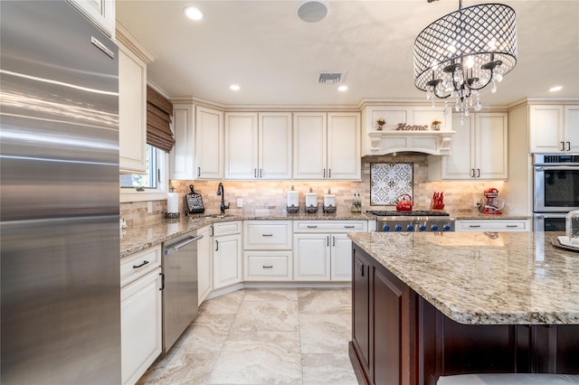 kitchen with hanging light fixtures, light stone counters, backsplash, a chandelier, and appliances with stainless steel finishes