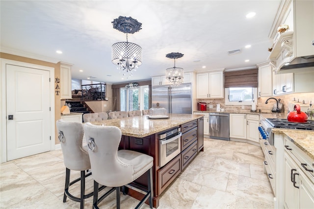 kitchen with pendant lighting, light stone countertops, appliances with stainless steel finishes, a kitchen island, and a breakfast bar area