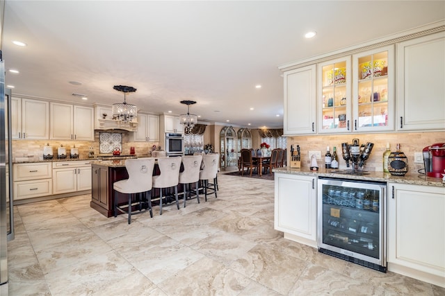 kitchen featuring stainless steel oven, hanging light fixtures, light stone counters, a breakfast bar area, and beverage cooler