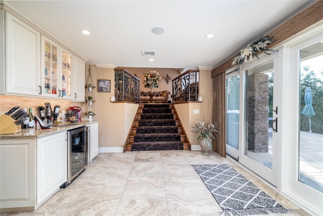 bar featuring light stone countertops, backsplash, ornamental molding, beverage cooler, and white cabinetry