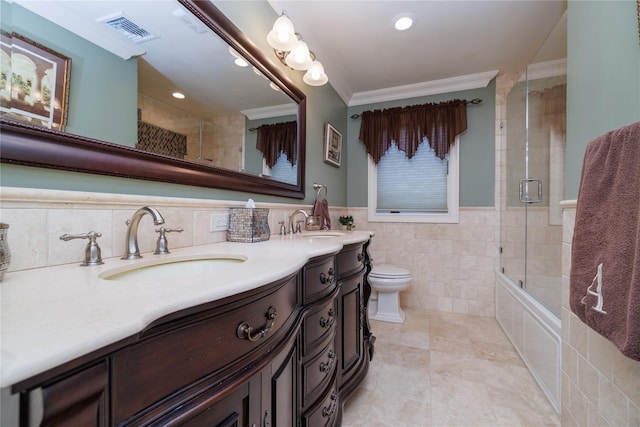 full bathroom featuring vanity, bath / shower combo with glass door, toilet, ornamental molding, and tile walls