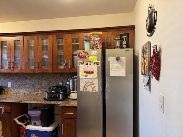 kitchen featuring decorative backsplash, stainless steel refrigerator, and dark stone counters