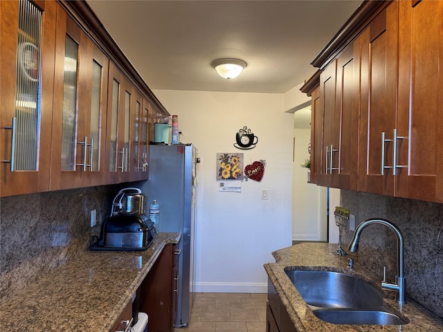 kitchen with decorative backsplash, dark stone counters, sink, light tile patterned floors, and stainless steel refrigerator