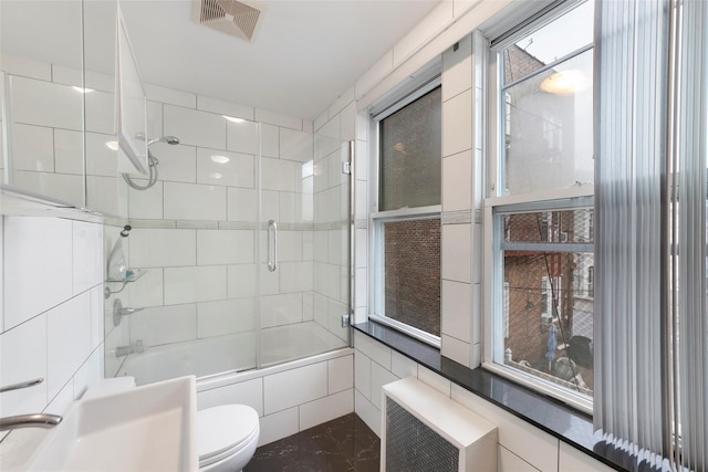 bathroom featuring combined bath / shower with glass door, radiator heating unit, toilet, and tile walls