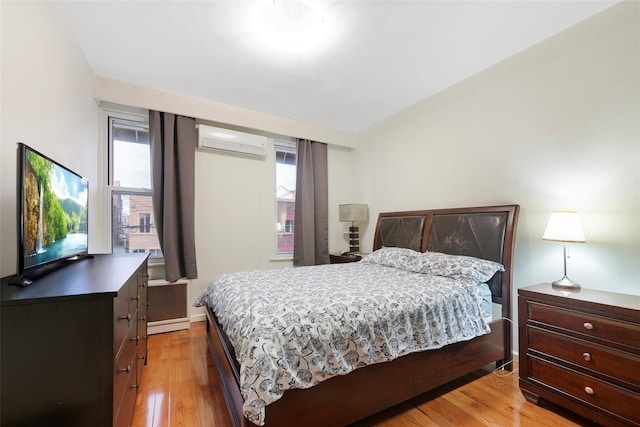 bedroom with a wall mounted air conditioner, light hardwood / wood-style floors, and multiple windows