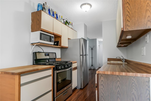 kitchen featuring butcher block countertops, stainless steel gas range oven, sink, and a textured ceiling