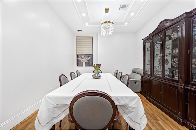 dining room with a chandelier, a tray ceiling, and light hardwood / wood-style flooring