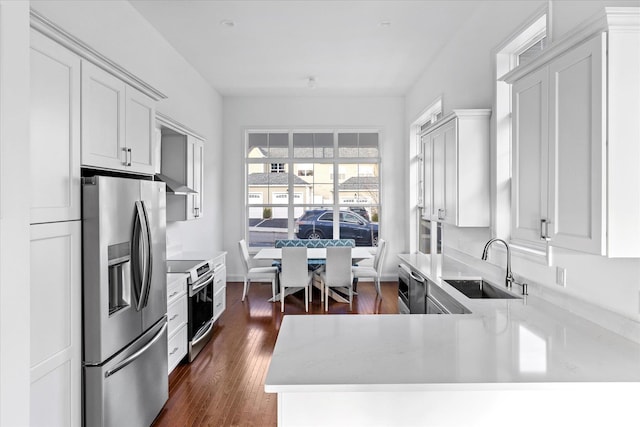 kitchen with kitchen peninsula, sink, wall chimney exhaust hood, appliances with stainless steel finishes, and white cabinetry