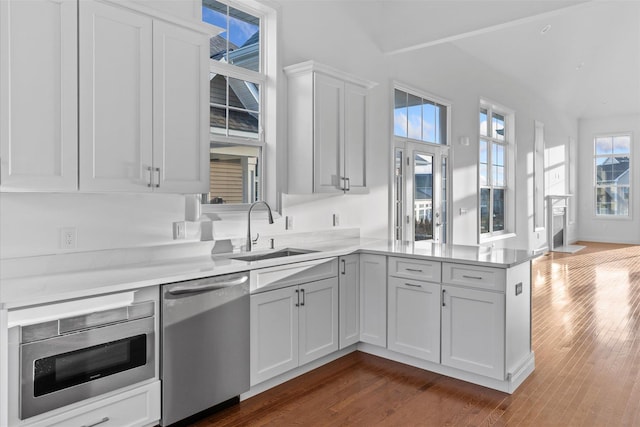 kitchen featuring sink, stainless steel dishwasher, dark hardwood / wood-style floors, kitchen peninsula, and white cabinets