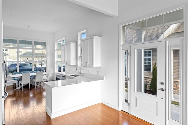 kitchen with hardwood / wood-style floors, white cabinetry, kitchen peninsula, and sink