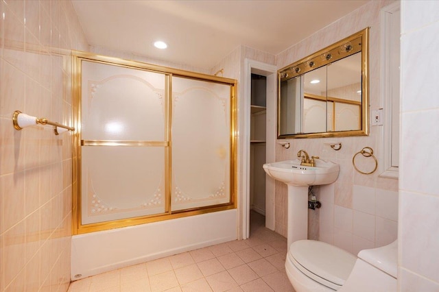 bathroom featuring toilet, combined bath / shower with glass door, and tile walls