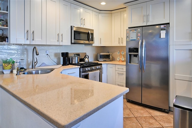 kitchen with kitchen peninsula, light tile patterned floors, light stone countertops, appliances with stainless steel finishes, and white cabinetry