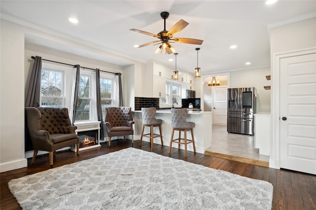 living area with ceiling fan, dark hardwood / wood-style floors, and ornamental molding