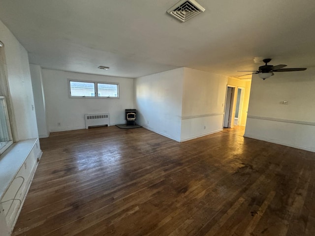 unfurnished living room with ceiling fan, a wood stove, radiator heating unit, and dark hardwood / wood-style floors