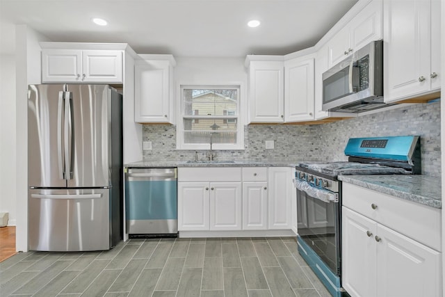 kitchen with decorative backsplash, sink, white cabinetry, appliances with stainless steel finishes, and light stone counters