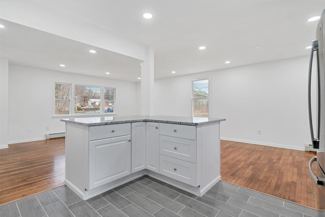 kitchen with a baseboard heating unit, stainless steel fridge, light stone counters, and white cabinetry