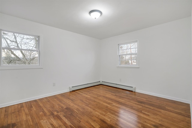 empty room with baseboard heating, a wealth of natural light, and hardwood / wood-style flooring