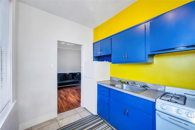 kitchen featuring light tile patterned floors, white appliances, blue cabinets, and sink