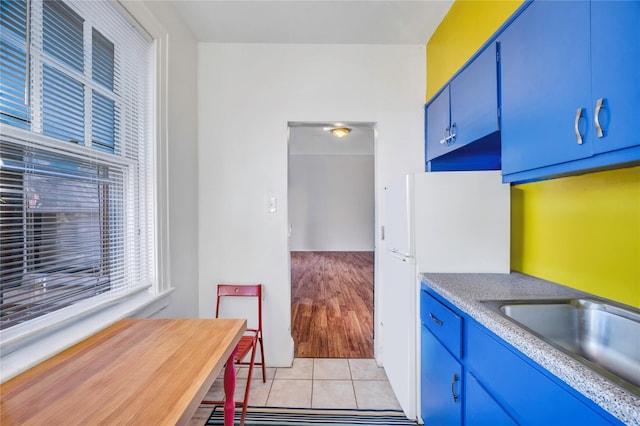 kitchen featuring blue cabinetry, white refrigerator, light tile patterned floors, and sink