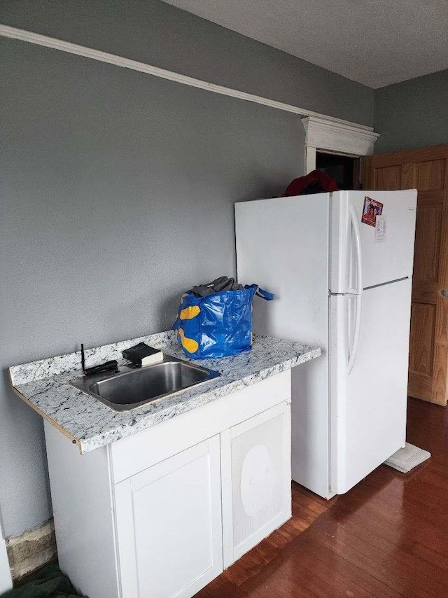 kitchen with dark hardwood / wood-style flooring, light stone counters, sink, white fridge, and white cabinetry